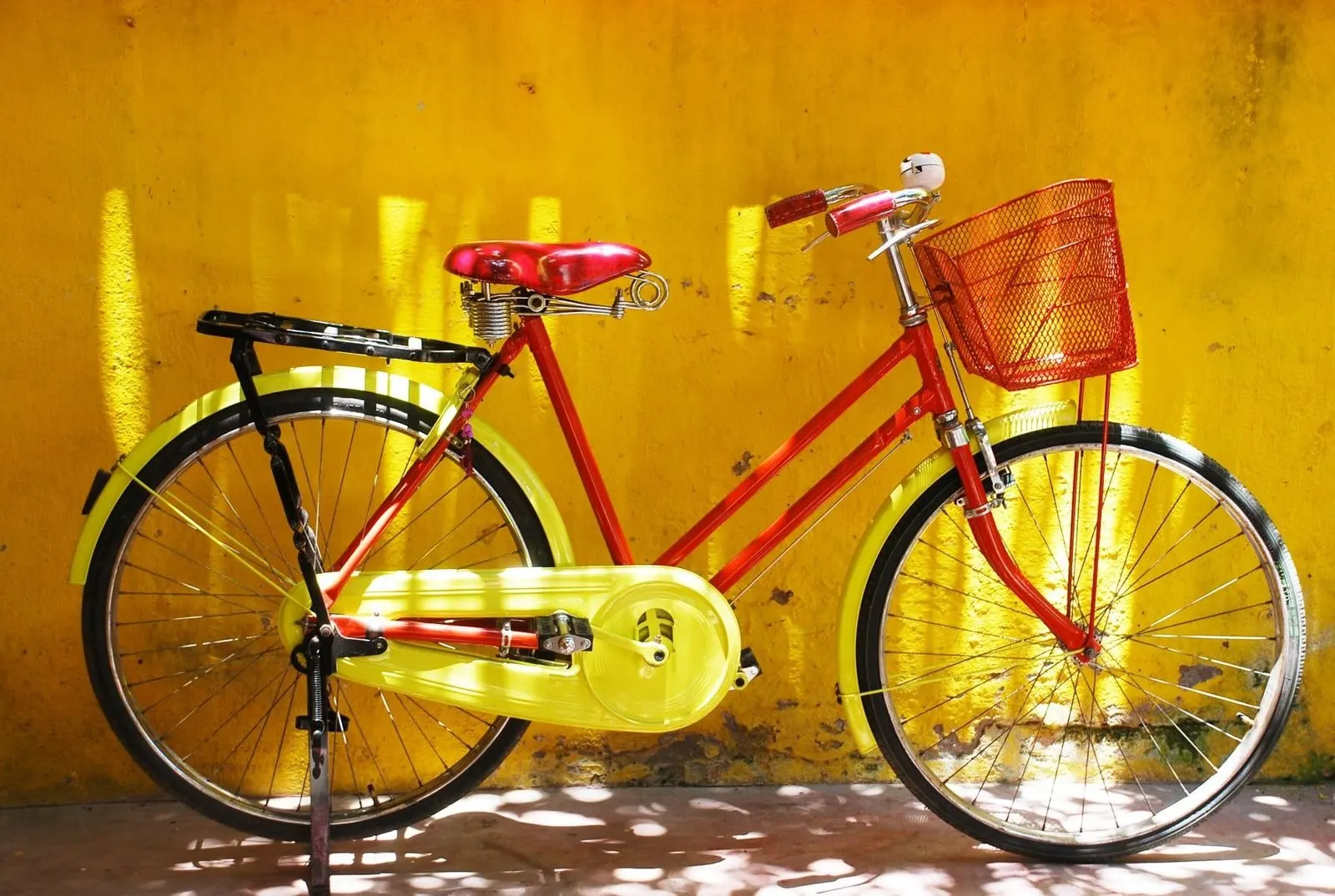 A red and lime-green vintage bicycle with a red basket in front of a golden yellow wall