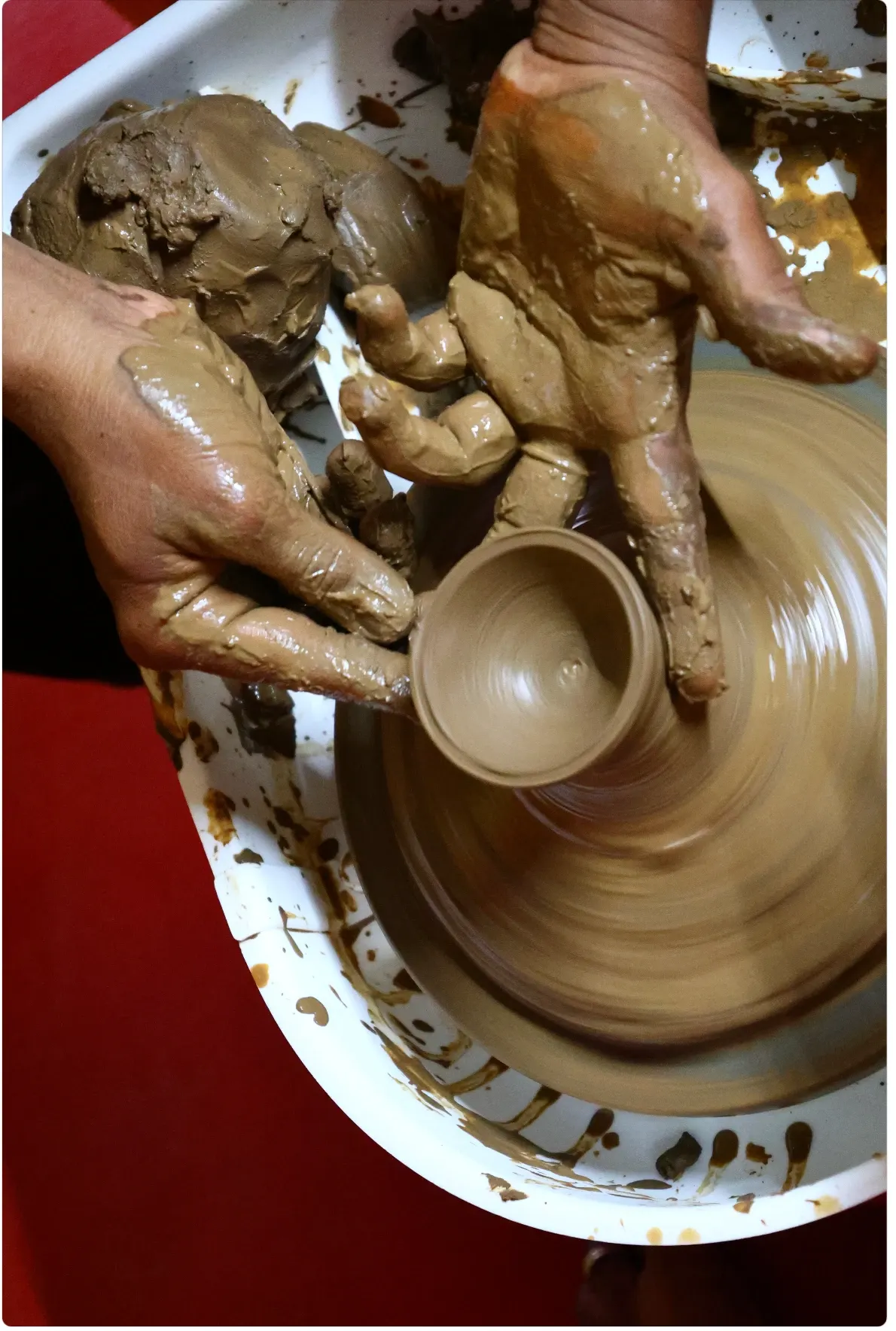 Clay-covered hands shape a small cup on a spinning pottery wheel