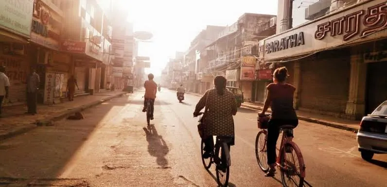 Two cyclists ride down a sunlit Pondicherry street in the early morning