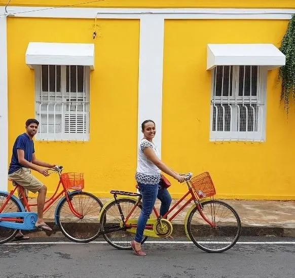 Two guests on colourful vintage bicycles in front of a yellow French-colonial wall